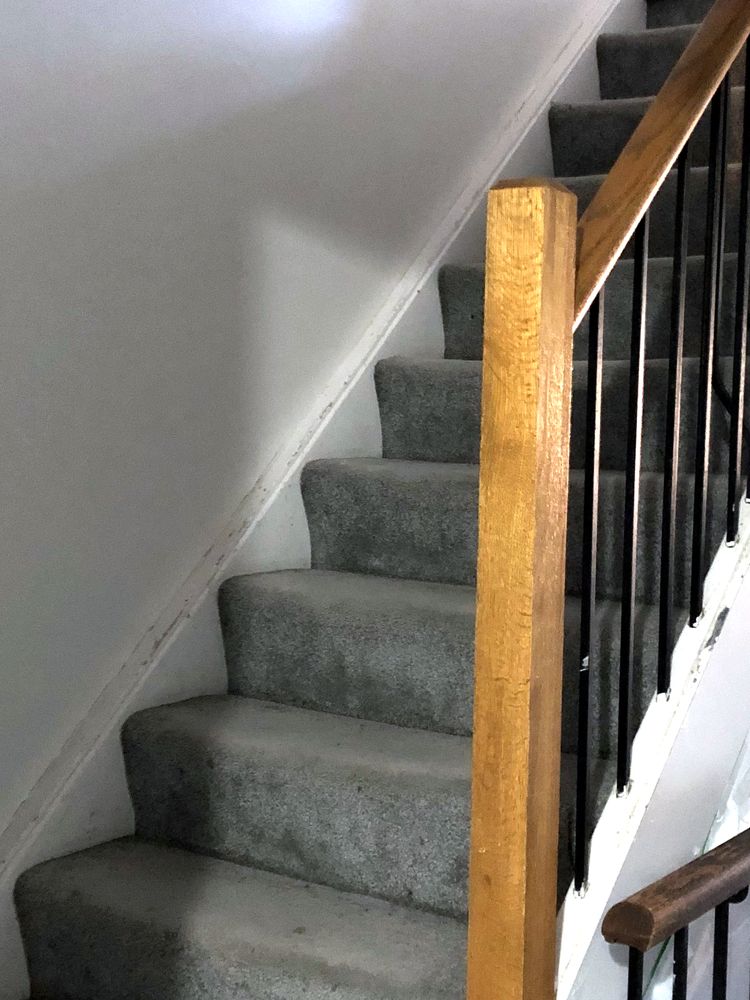 Grey carpet on a staircase with an oak newel post and black metal spindles