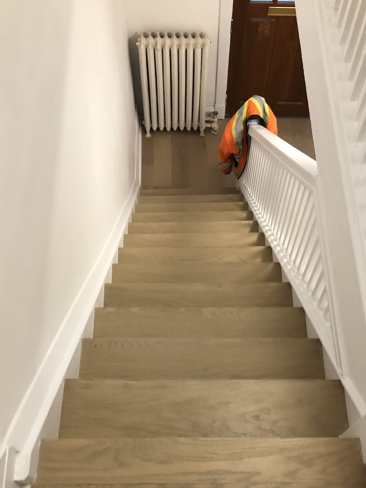Interior staircase with new light wood treads matching the floor below and a white painted railing