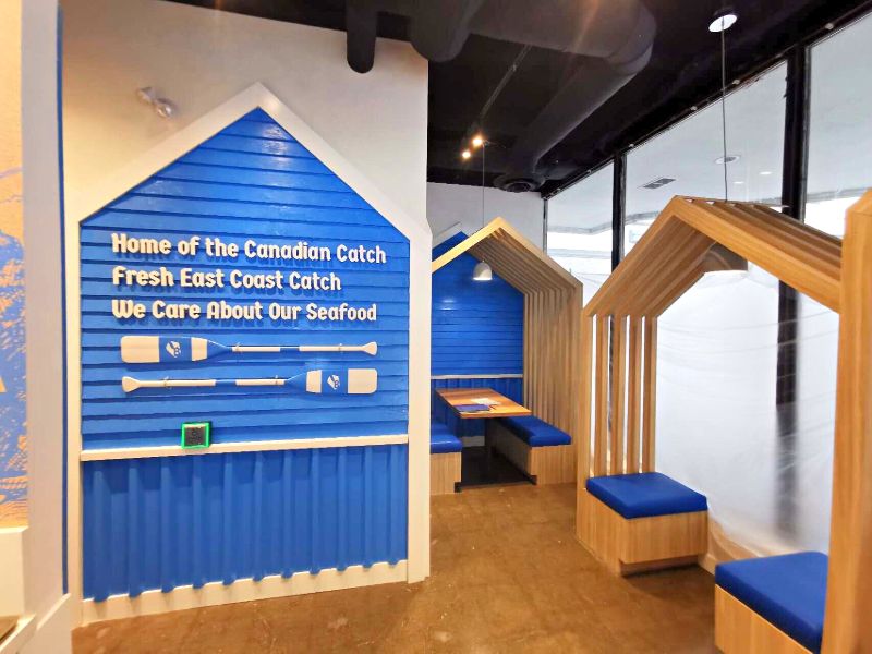 House-shaped wood booths beside a blue siding wall with lettering and oars