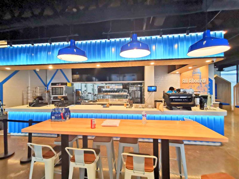 Lit blue corrugated service counter with three blue pendant lights and the kitchen behind