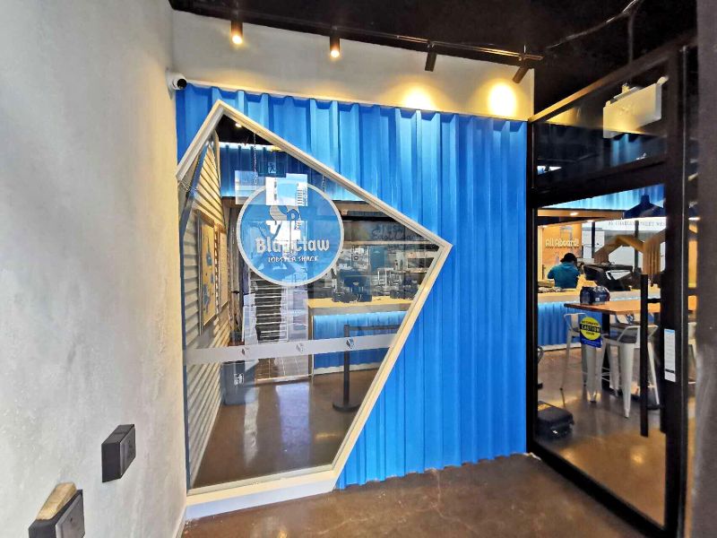 Entrance vestibule with a blue corrugated wall and an angled window into the restaurant