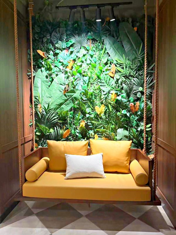 Swing seat with yellow leather cushions in front of a green plant wall
