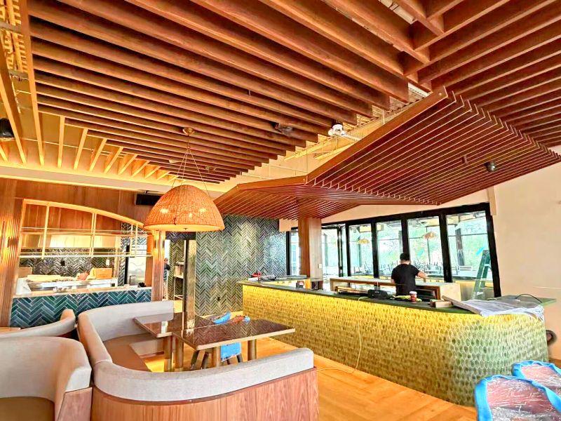 Bar with a green fish-scale tile front under a stepped slatted ceiling