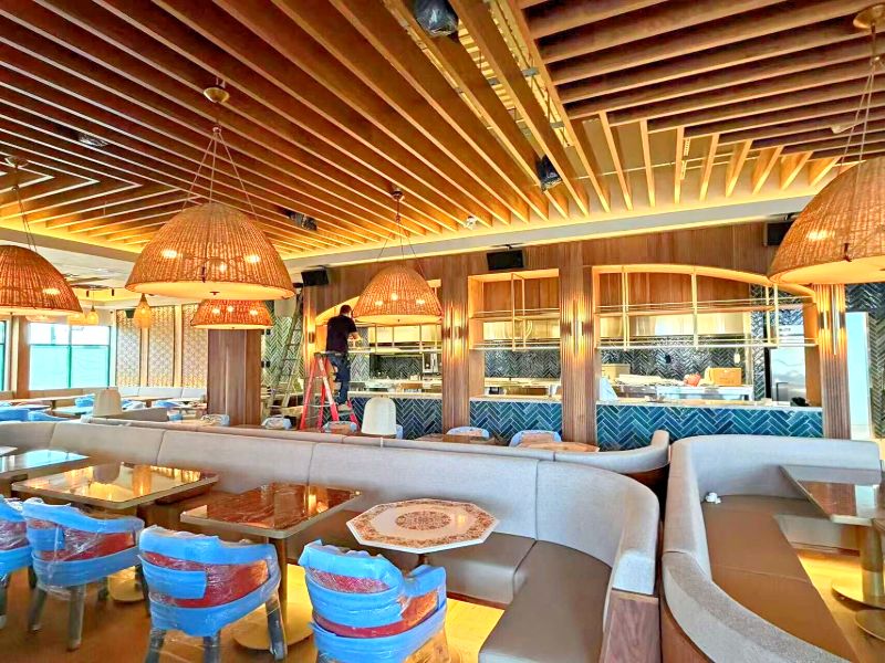 Curved booths under woven pendants, with the open kitchen behind