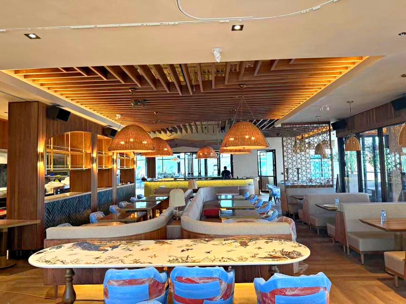 Dining room under a slatted wood ceiling with woven pendant lights and a long painted table