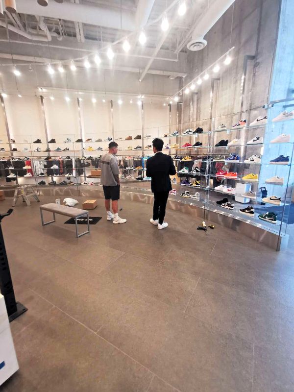 Sneaker store with a curved wall of glass shelves and track lighting, being set up